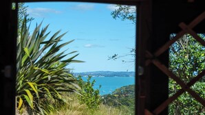 A view through a window with a view of a coastal landscape, including greenery and a body of water with boats.