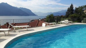 A swimming pool with lounge chairs, a view of a lake, and mountains in the background.