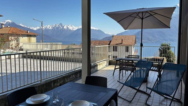 A terrace with a table set for two, a chair, and an umbrella, overlooking a mountain landscape. - The Wave Musso - Larihome A87 (Musso)