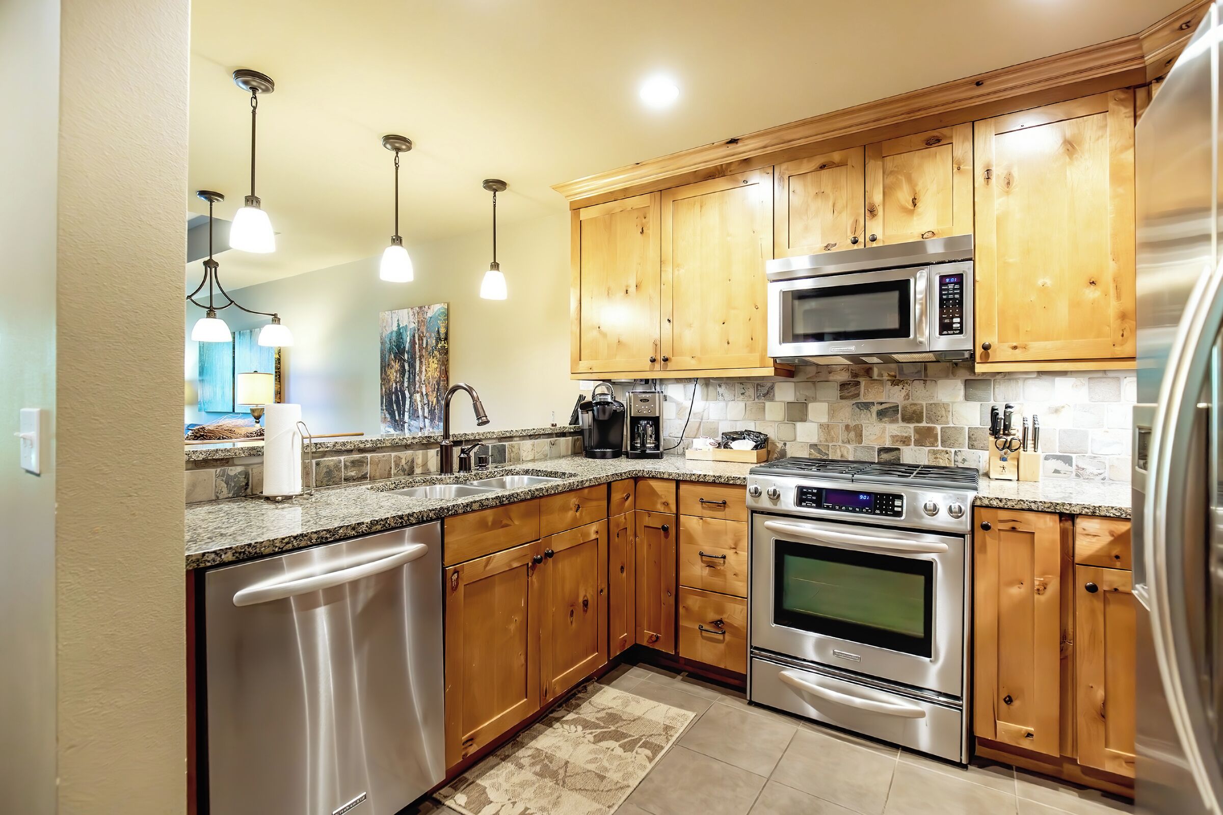 A modern kitchen with wooden cabinets, stainless steel appliances, granite countertops, and pendant lighting.