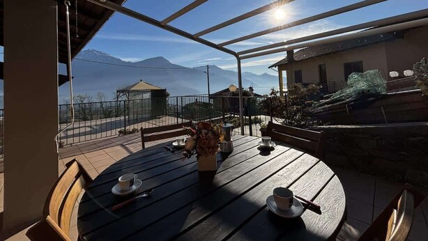 Une terrasse avec une table dressée pour deux personnes, un vase de fleurs et une vue sur les montagnes.
