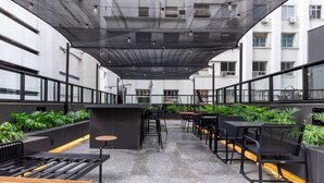 An outdoor seating area with tables and chairs, a bar counter, and planters with greenery.