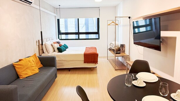 A modern living room with a sofa, a dining table set for two, and a TV mounted on the wall.