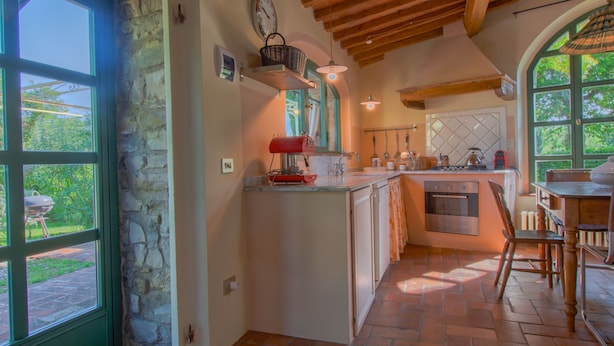 Una cocina con pared de piedra, vigas de madera, un ventanal grande y un comedor con mesa y sillas.