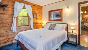 A wooden-paneled bedroom with a bed, two bedside lamps, and a window with curtains. - Keuka Lakefront | Dock w/ Boat Access | Kayak (Hammondsport)