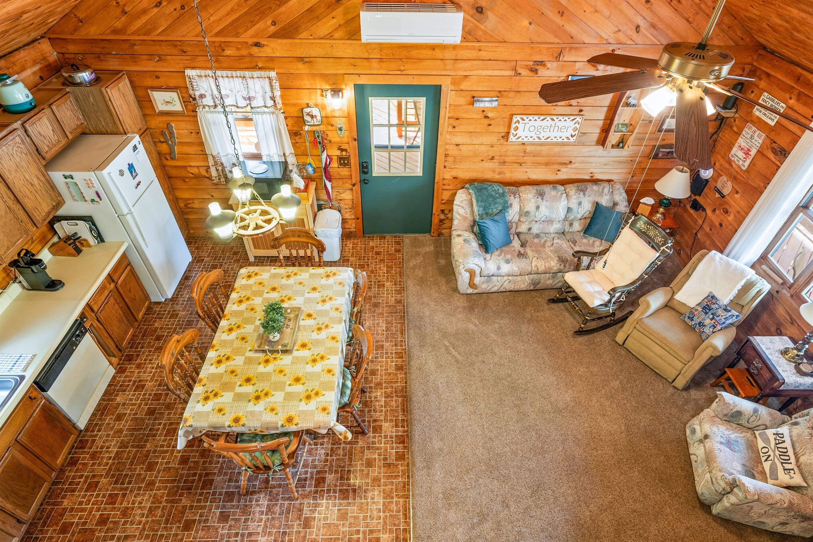 A cabin interior with a dining table, wooden walls, a ceiling fan, and a cozy seating area.