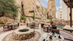 Ein Essbereich im Freien mit Steintischen und -stühlen, einer Feuerstelle und einem Pool.