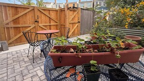 A patio area with a wooden fence, a round table, two chairs, and a planter box with plants.