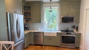 A kitchen with a stainless steel refrigerator, dishwasher, double oven, and a window with a view of greenery.