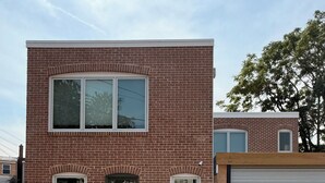 A two-story brick building with a green door, two windows on the ground floor, and a garage door.
