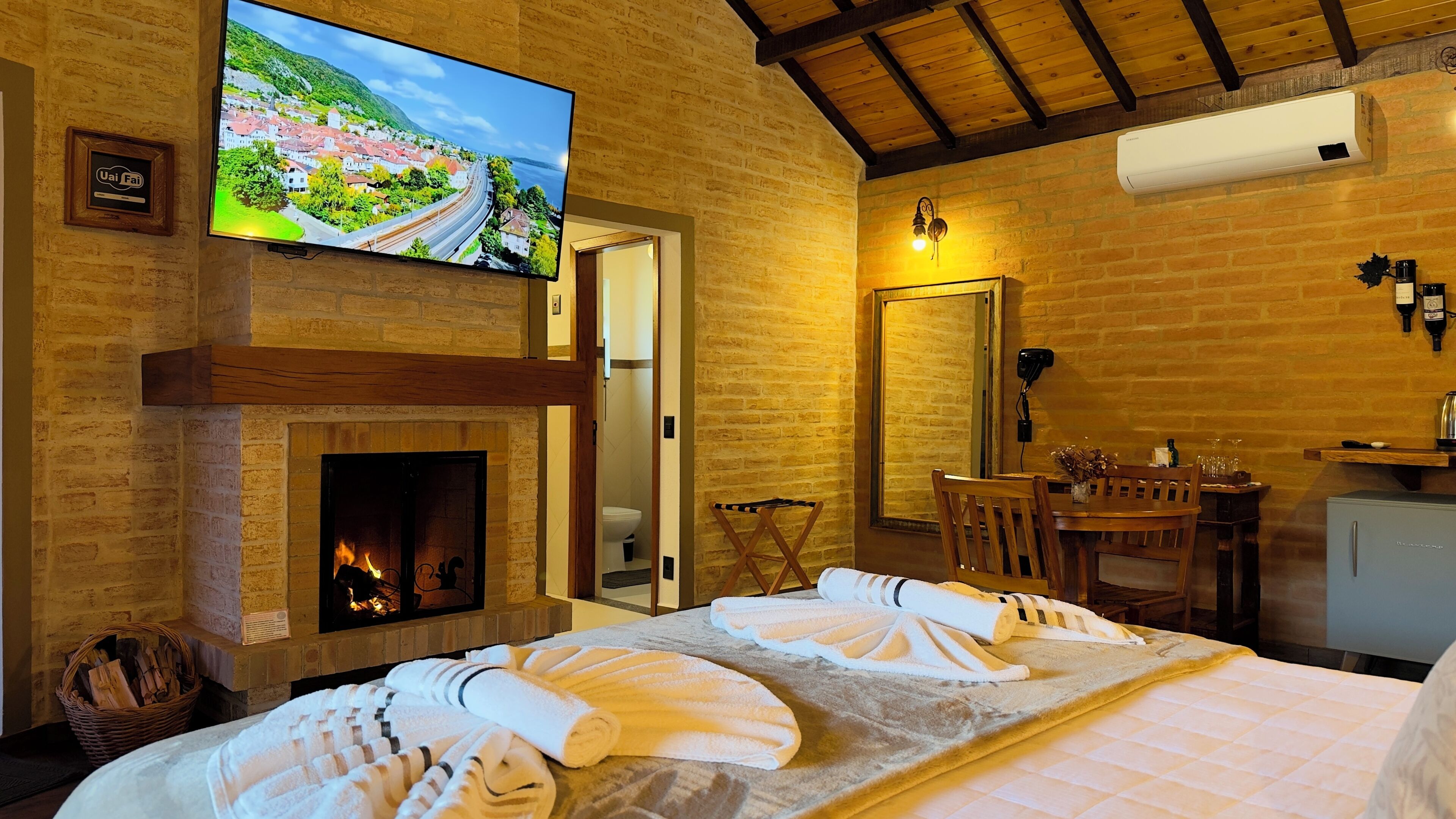 Una habitación de hotel con chimenea, televisor montado en la pared, comedor con mesa y sillas, y cama con toallas.