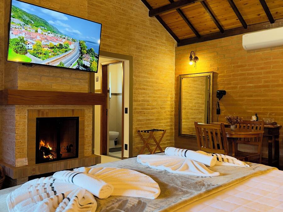 Una habitación de hotel con chimenea, televisor montado en la pared, comedor con mesa y sillas, y cama con toallas.