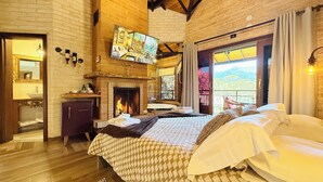 A bedroom with a fireplace, a bed, a TV, and a balcony with a view. - Flores da Mantiqueira (Monte Verde)