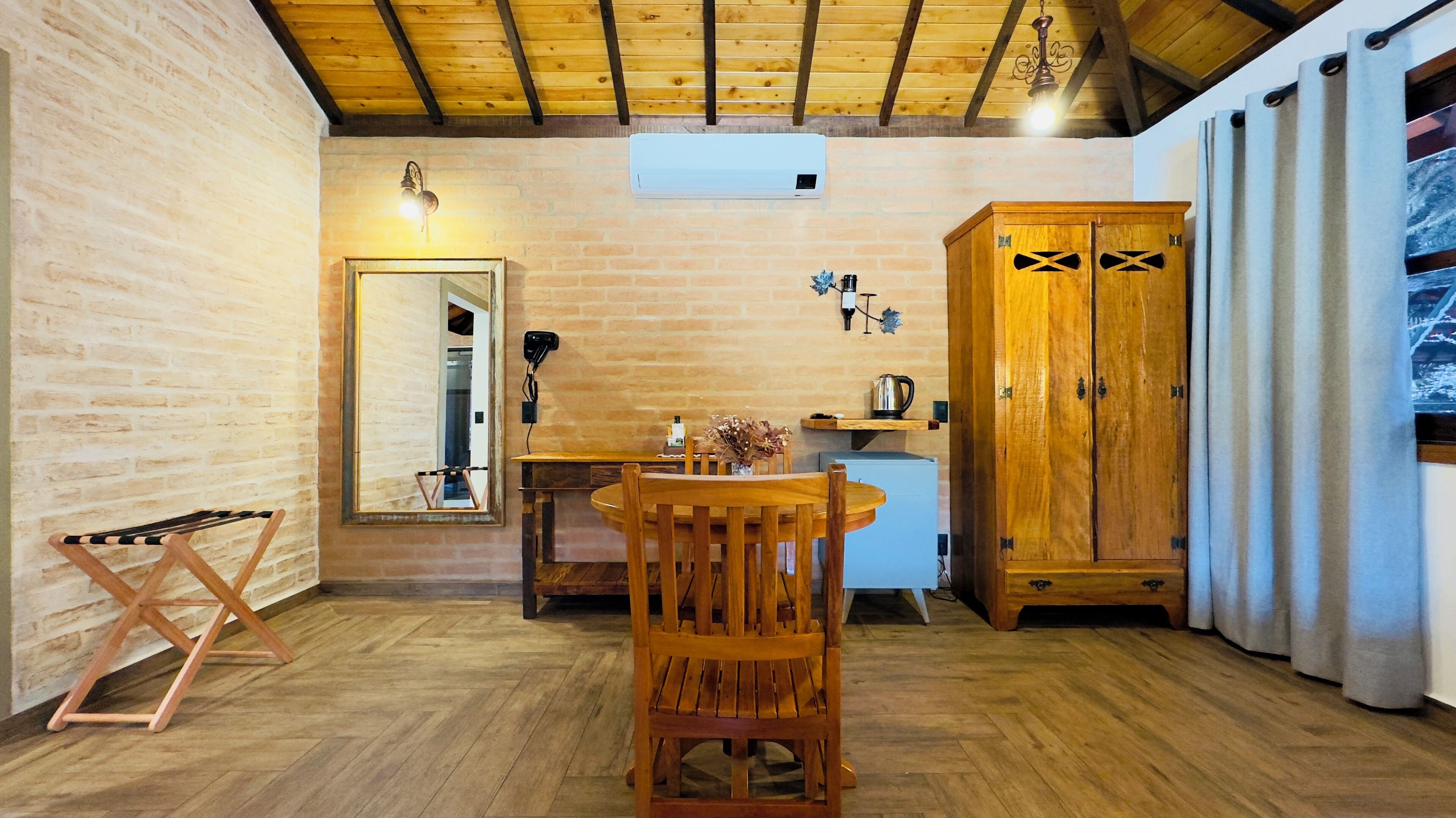 A cozy room with a wooden table, chairs, a cabinet, and a mirror on brick walls.
