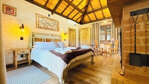 A cozy bedroom with a wooden bed, a nightstand, a wall-mounted lamp, and a large window with curtains. - Flores da Mantiqueira (Monte Verde)