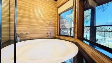 A modern bathroom with a freestanding bathtub, wooden paneling, and large windows offering a view of the outdoors.