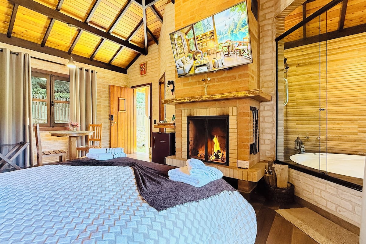 A spacious bedroom with a large bed, a fireplace, a bathroom with a bathtub, and a dining area with a table and chairs.