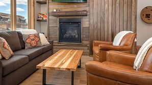 A cozy living room with a fireplace, a sofa, a leather armchair, and a wooden coffee table. - New! Condo Downtown with rooftop patio, steam shower, mountain views (Whitefish)
