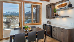 Een moderne keuken met houten kastjes, een eettafel met stoelen en uitzicht op bergen door grote ramen.