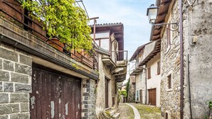 A narrow cobblestone street flanked by stone buildings with wooden shutters and a metal gate.