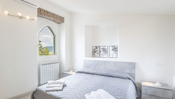 A modern bedroom with a bed, a nightstand, a mirror, and a window with a view.