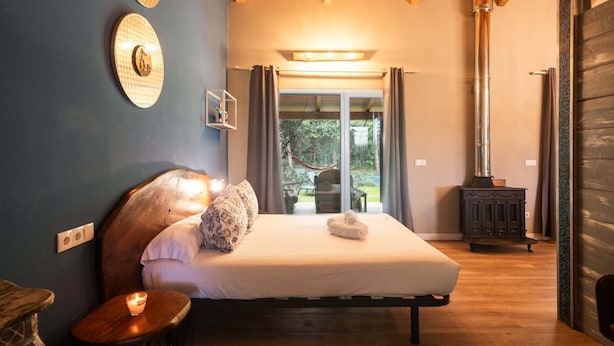 A bedroom with a bed, bedside table, and a view of the outdoors.