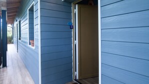 A covered porch with wooden beams, a blue exterior wall, and a door leading to a room.