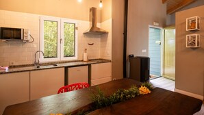 Une cuisine avec des meubles blancs, un four à micro-ondes, une cuisinière et un évier. On y trouve une chaise rouge et une table en bois décorée de fleurs.
