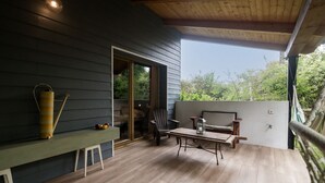 Un balcon avec une table et des chaises en bois, un fauteuil suspendu et un grand vase.