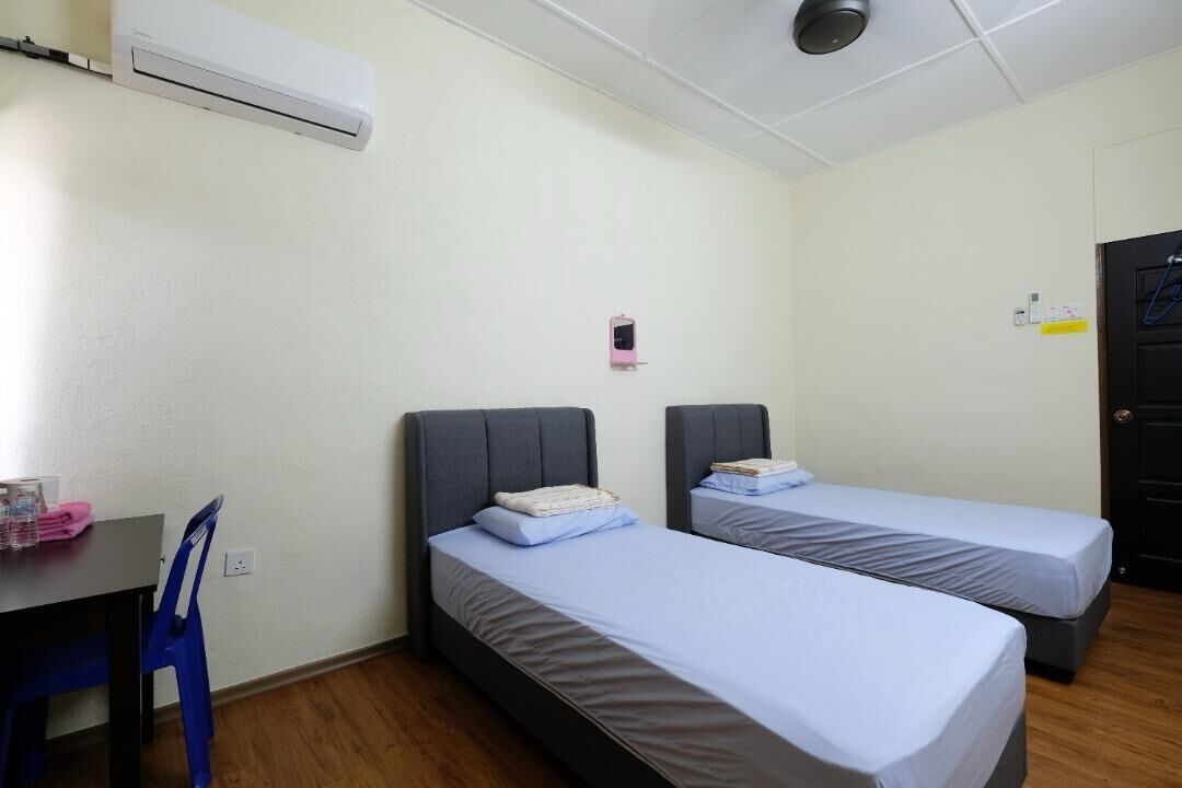 A small, clean room with two single beds, a desk, and a chair.