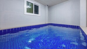 Une piscine aux carreaux bleus, une fenêtre à cadre blanc et des murs blancs.