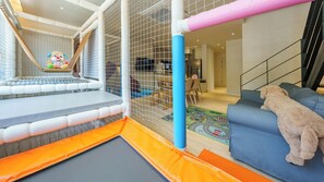 Un área de juegos interior con una zona de juegos suaves, un tobogán y un recinto cubierto de red.
