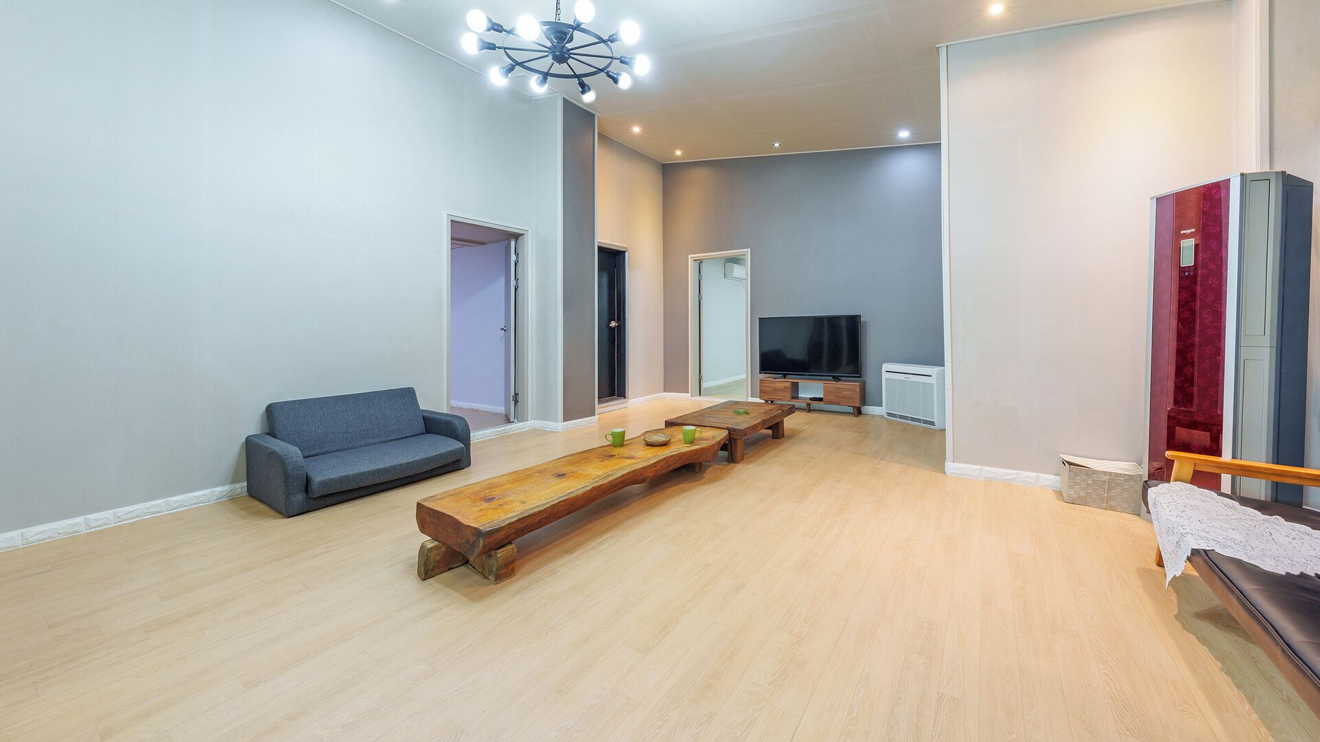 A modern living room with a sofa, a wooden coffee table, a TV, and a red door.