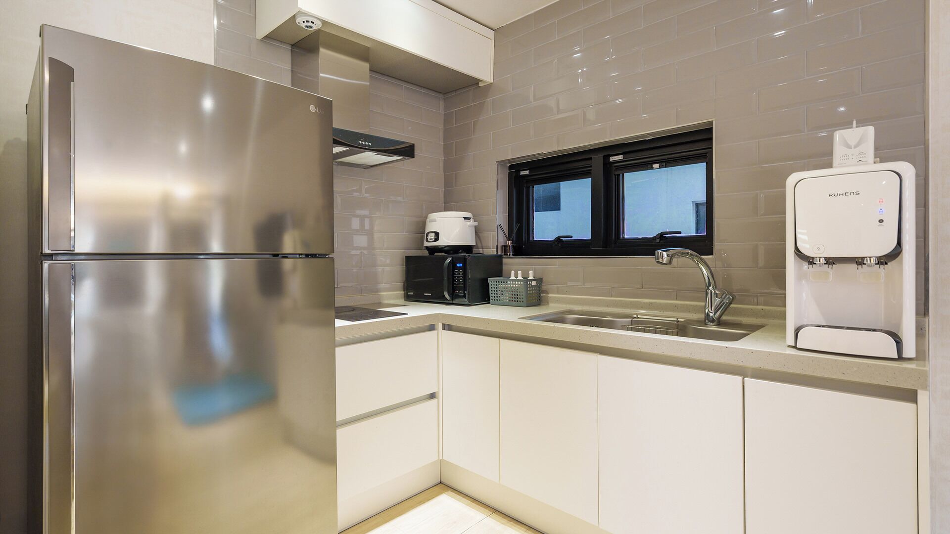 Una cocina moderna con un refrigerador de acero inoxidable, una cafetera, un microondas, un lavamanos y un dispensador de agua RuHens.