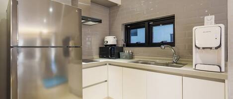 Una cocina moderna con un refrigerador de acero inoxidable, una cafetera, un microondas, un lavamanos y un dispensador de agua RuHens.