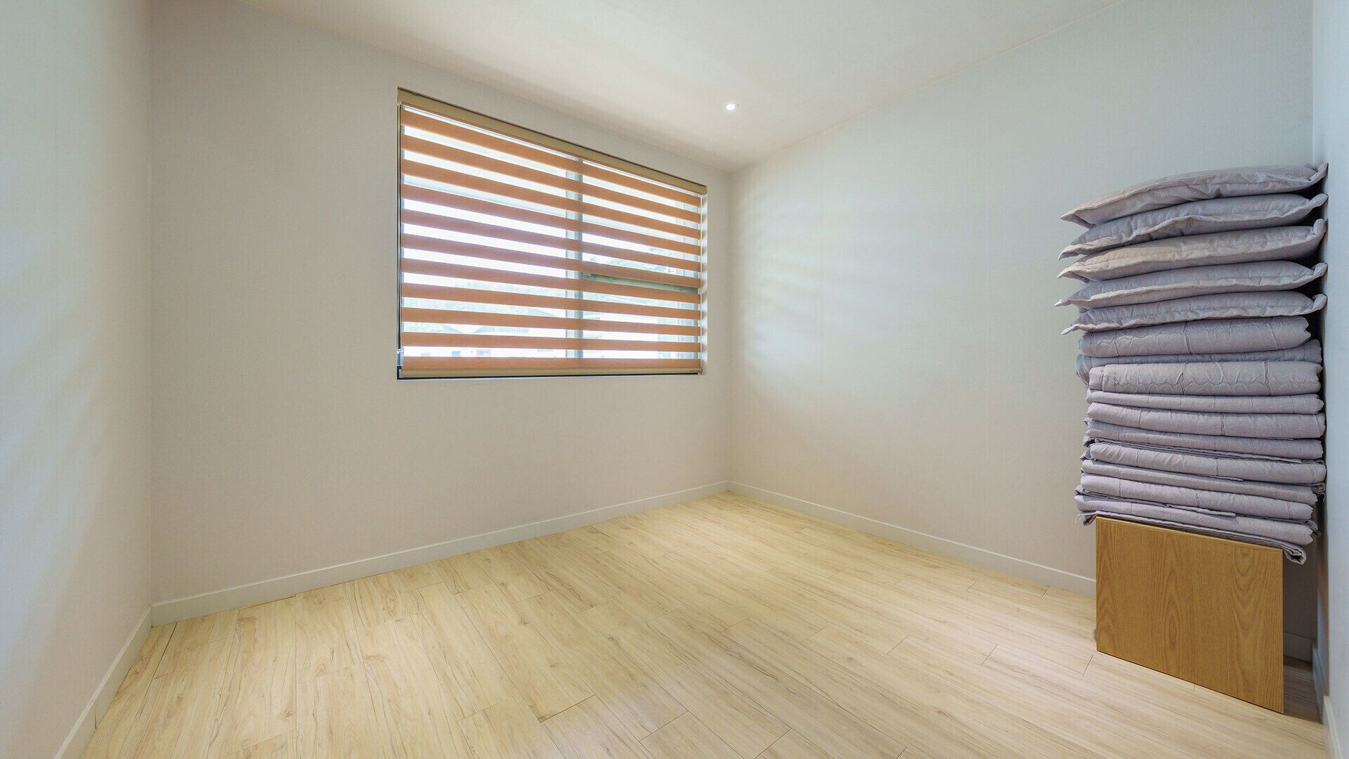 A room with a window, wooden flooring, and a stack of folded blankets.