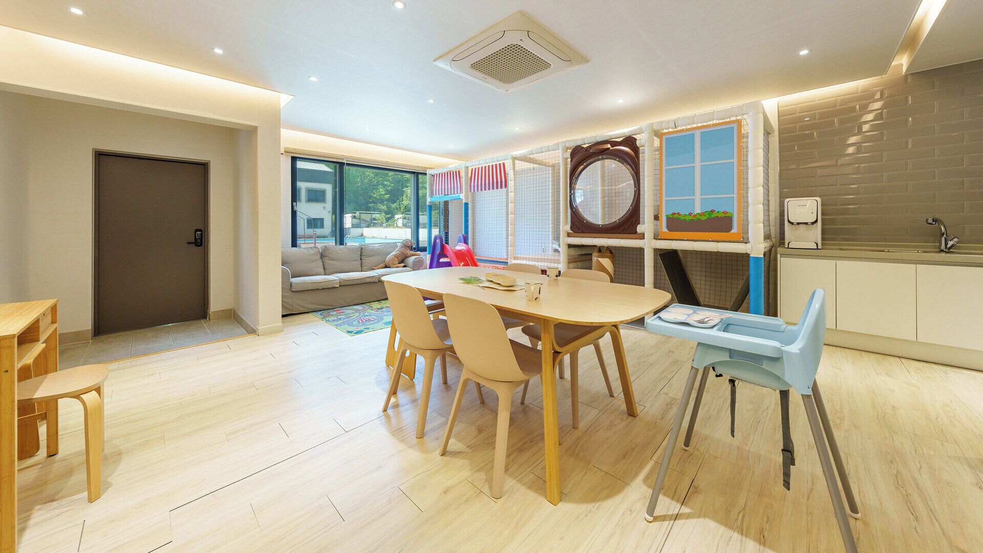 A modern kitchen with a dining area, large windows, and a view of the outdoors.