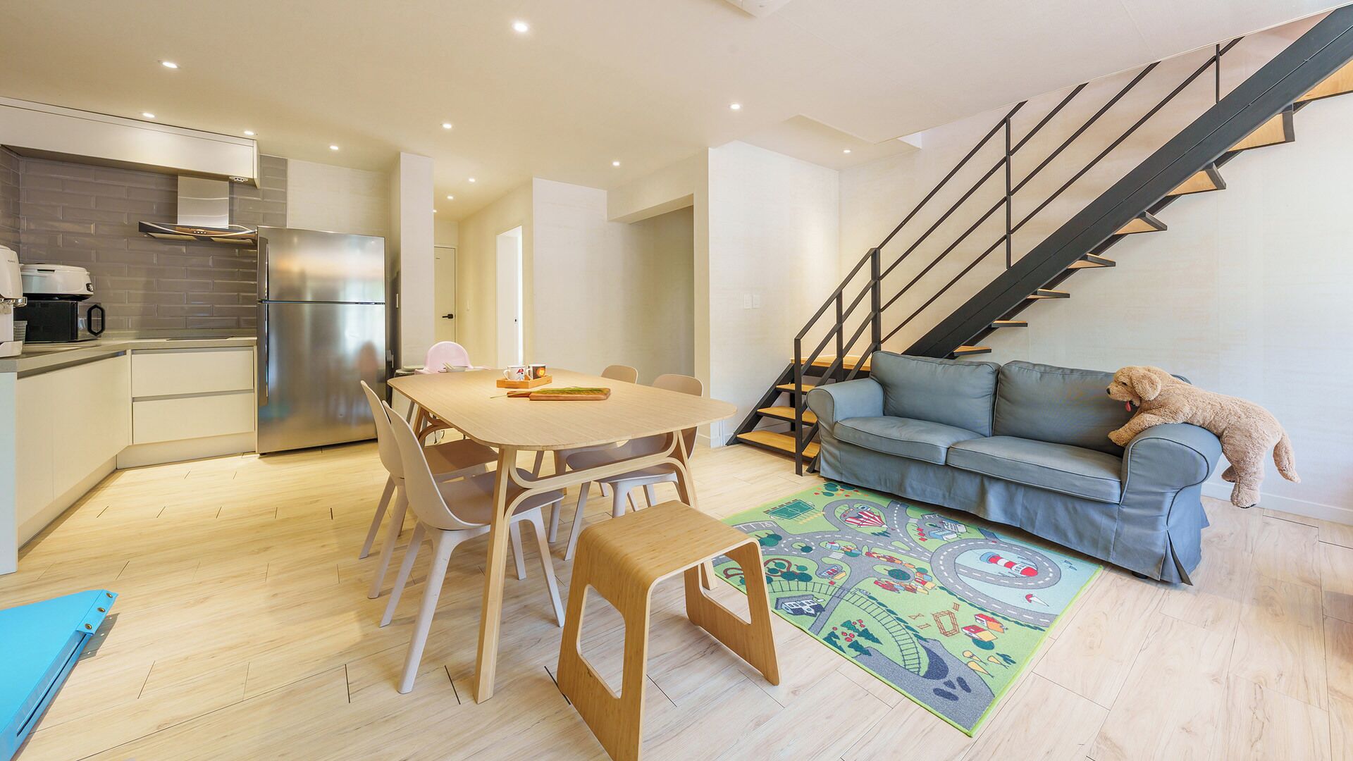 A modern interior with a dining area, kitchen, staircase, and a sofa with a dog.