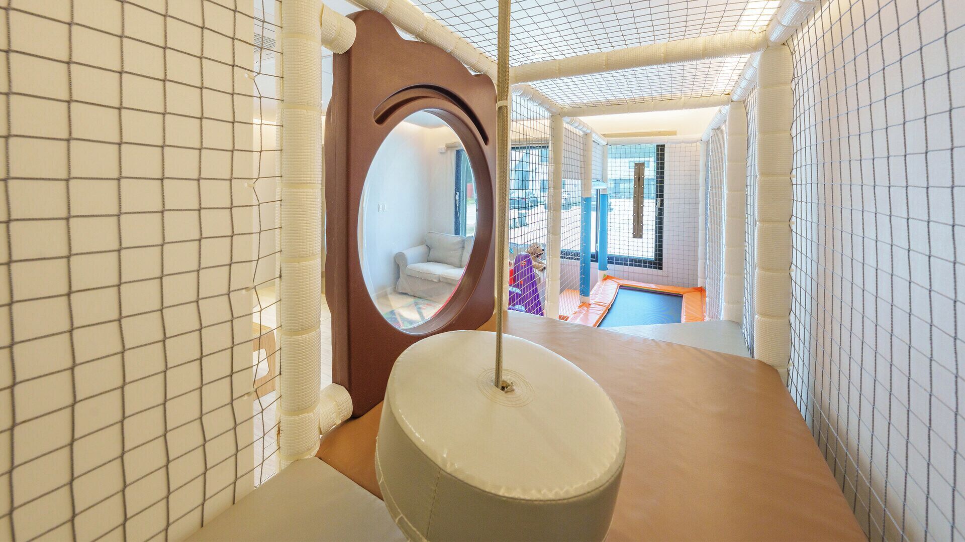 A play area with a climbing structure, a circular window, and a soft play surface.