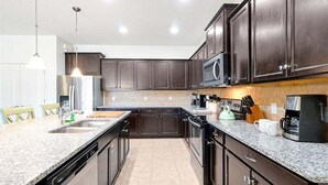 Uma cozinha moderna com armários escuros, bancadas de granito, geladeira de aço inoxidável e micro-ondas.
