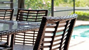 Uma mesa de jantar em vime com cadeiras, um tampo de vidro e vista para uma piscina.