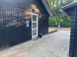Ein modernes Gebäude mit dunkler Fassade, einer weißen Tür und einem kleinen Vordach.