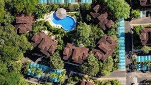 Oversigtsbillede af et resort med flere huse i bungalowstil, en central swimmingpool og frodig vegetation omkring.