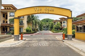 A gated entrance to a hotel with a yellow archway labeled 'The Oaks.' - The Oaks Tamarindo Luxury Condominium (provincia de guanacaste)