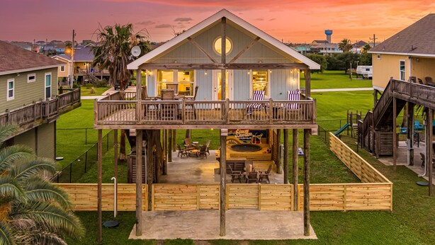 A two-story wooden structure with a balcony, outdoor seating, and a play area. - Steps to the Beach l Pool l Tiki Bar & Pet-Friendly (Crystal Beach)