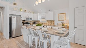 A modern kitchen with white cabinetry, stainless steel appliances, a granite island with bar stools, and a decorative backsplash. - Steps to the Beach l Pool l Tiki Bar & Pet-Friendly (Crystal Beach)