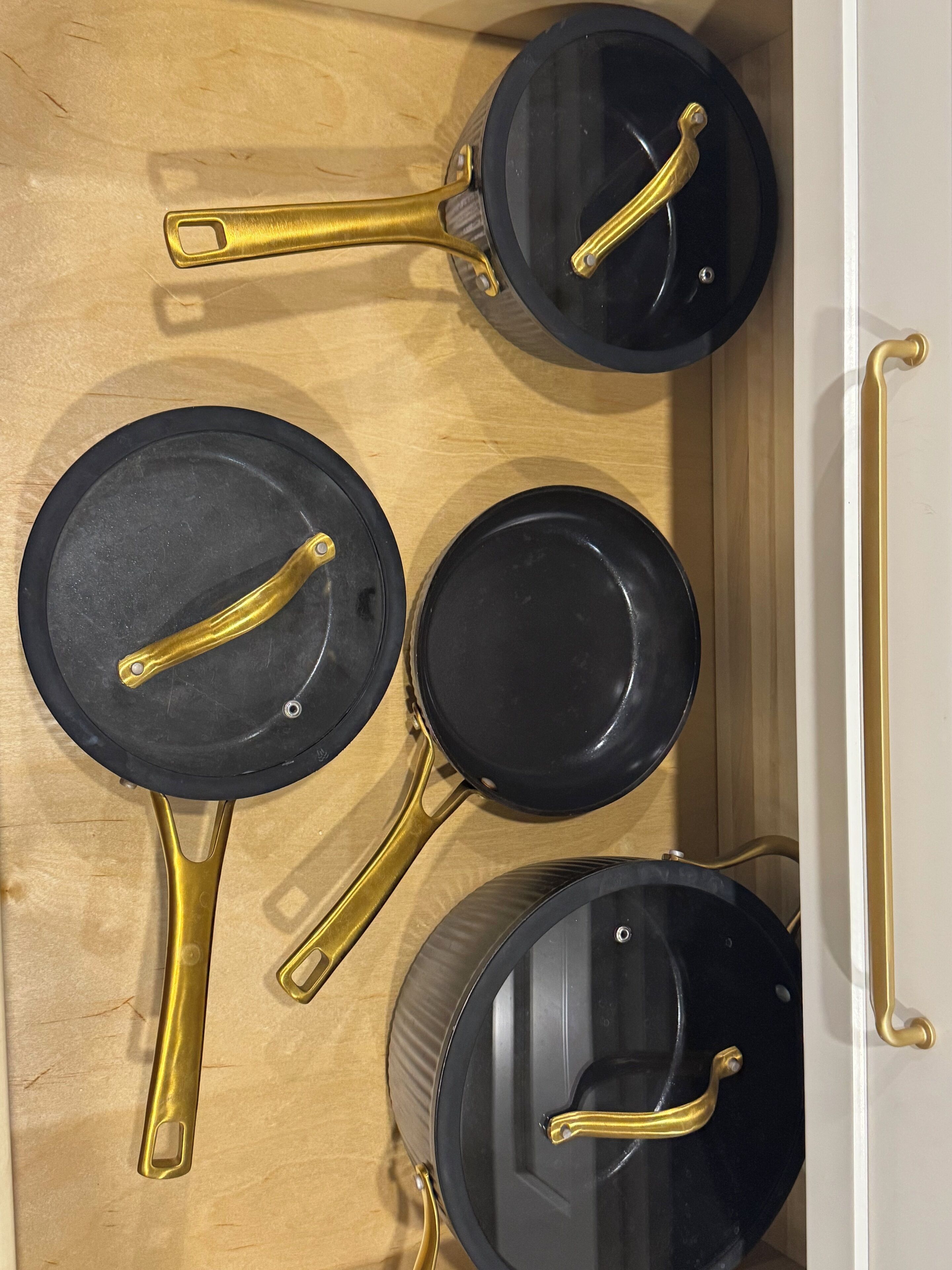 A kitchen drawer with four black frying pans with gold handles.