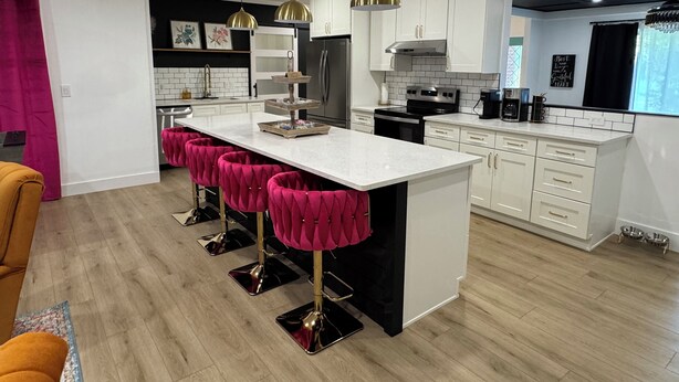 A modern kitchen with a central island, white cabinets, and pendant lighting.