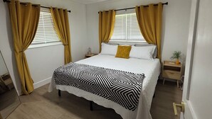 A bedroom with a bed, curtains, a nightstand, a ceiling fan, and a window with blinds.