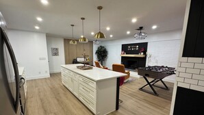 A modern kitchen with a central island, pendant lighting, and a foosball table.